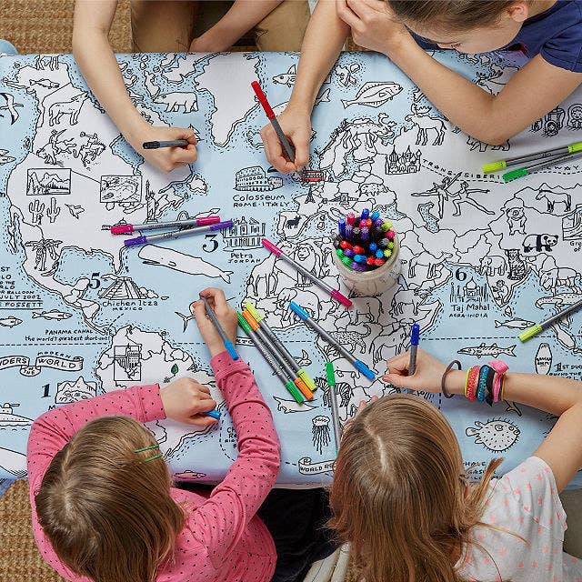 Four kids sit around the World Map Coloring Tablecloth, coloring in with markers