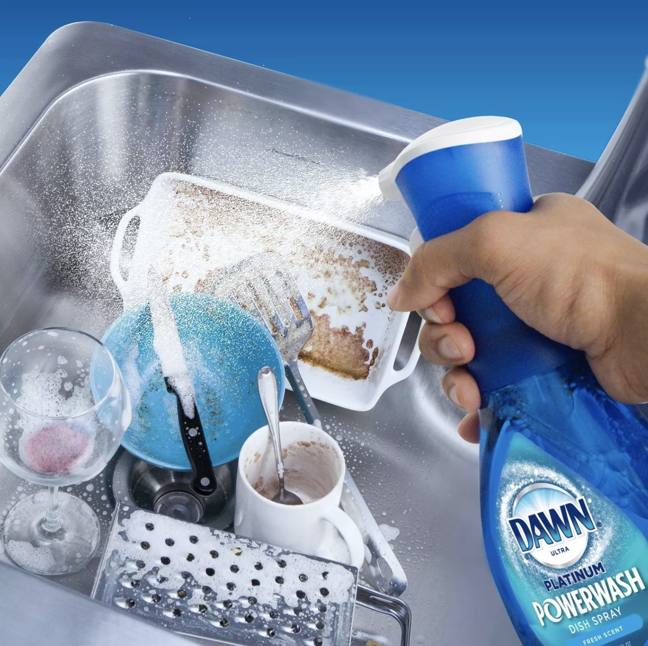 Hand holds blue bottle of Dawn Dish Spray over a sink filled with cups, plates, and utensils