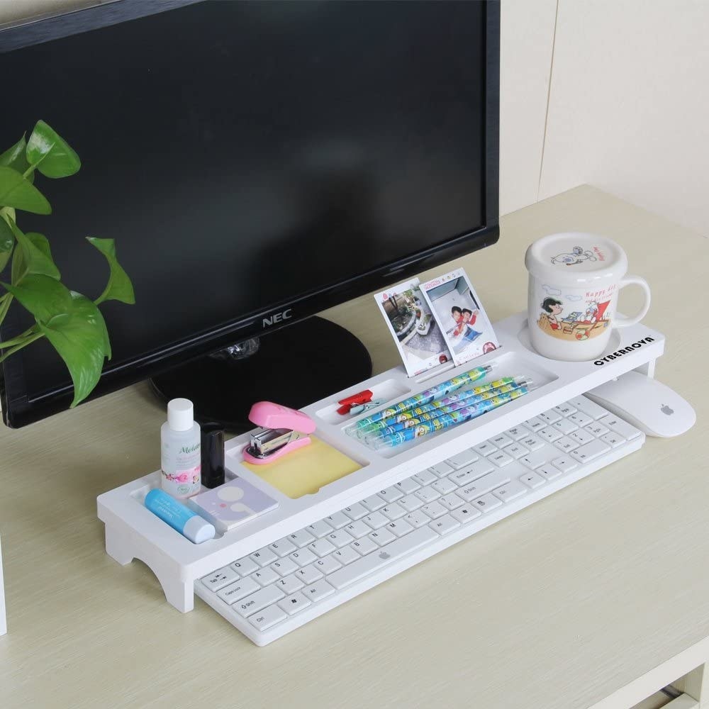 A long rectangular stand placed over a keyboard on a desk. The stand has a coffee mug, pens, pictures, a stapler, and lip balm organized neatly on top