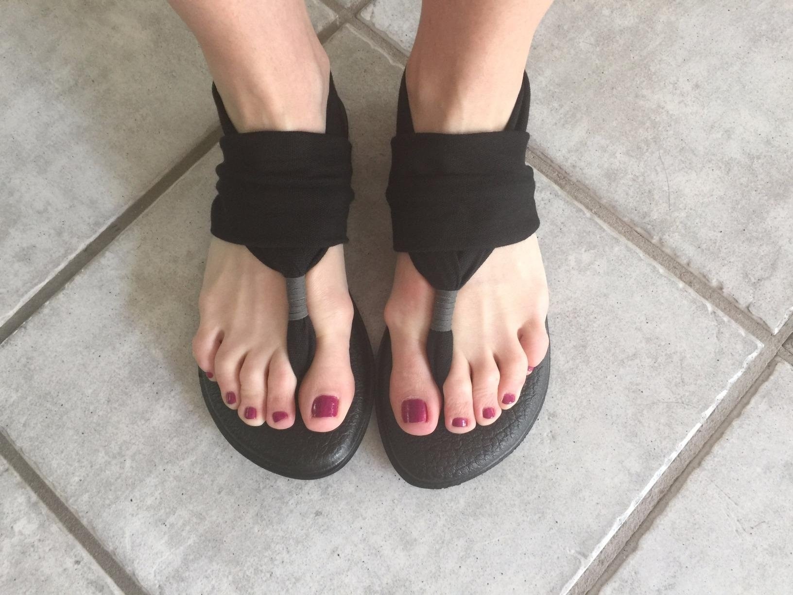 A reviewer's feet in the black thong-style sandals