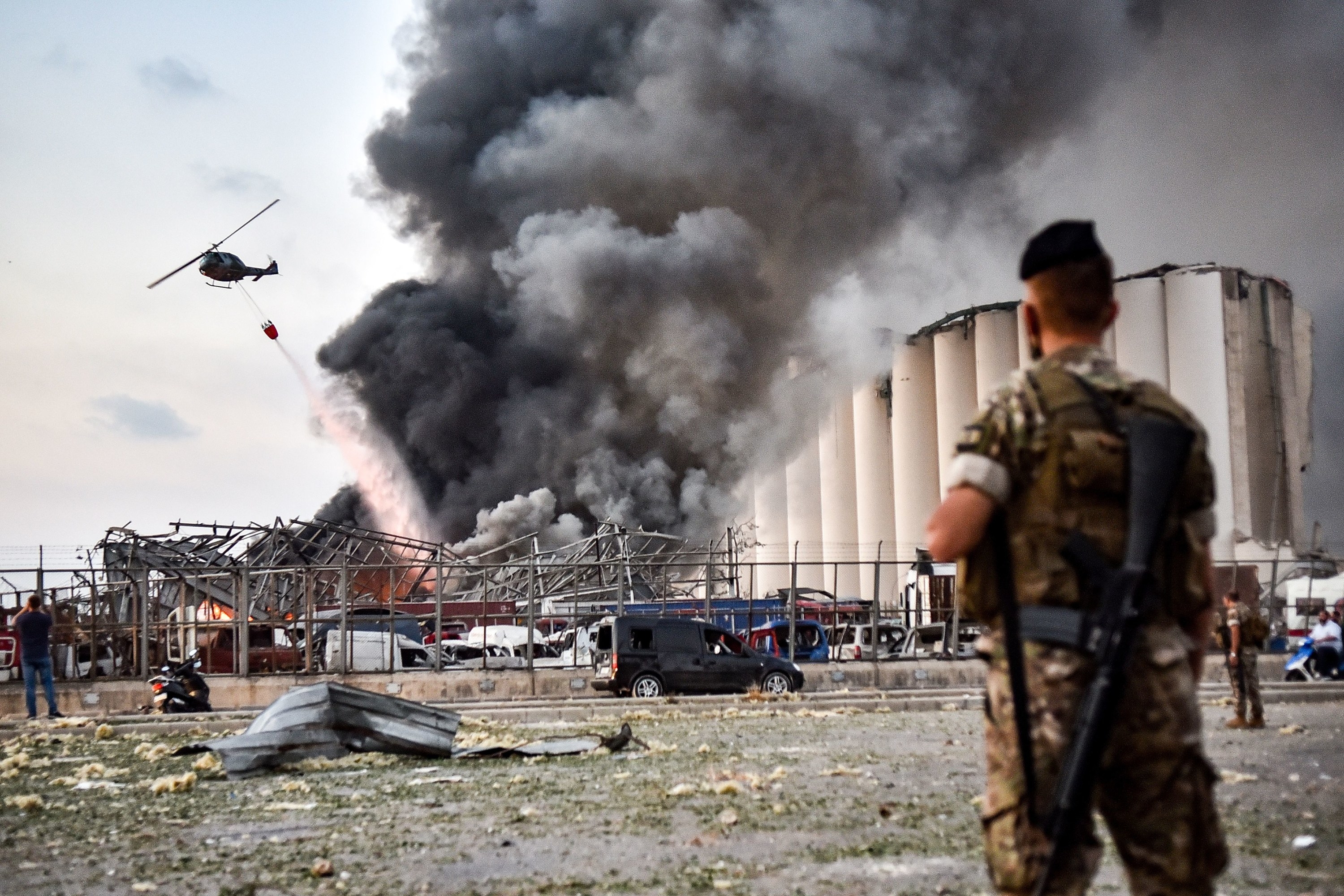 A helicopter douses flames and smoke next to a grain silo
