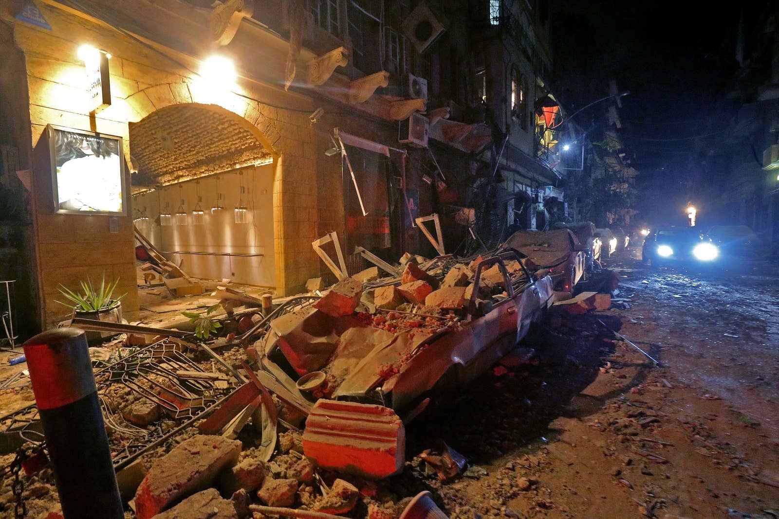 Cars are buried in rubble and buildings destroyed on a street at night