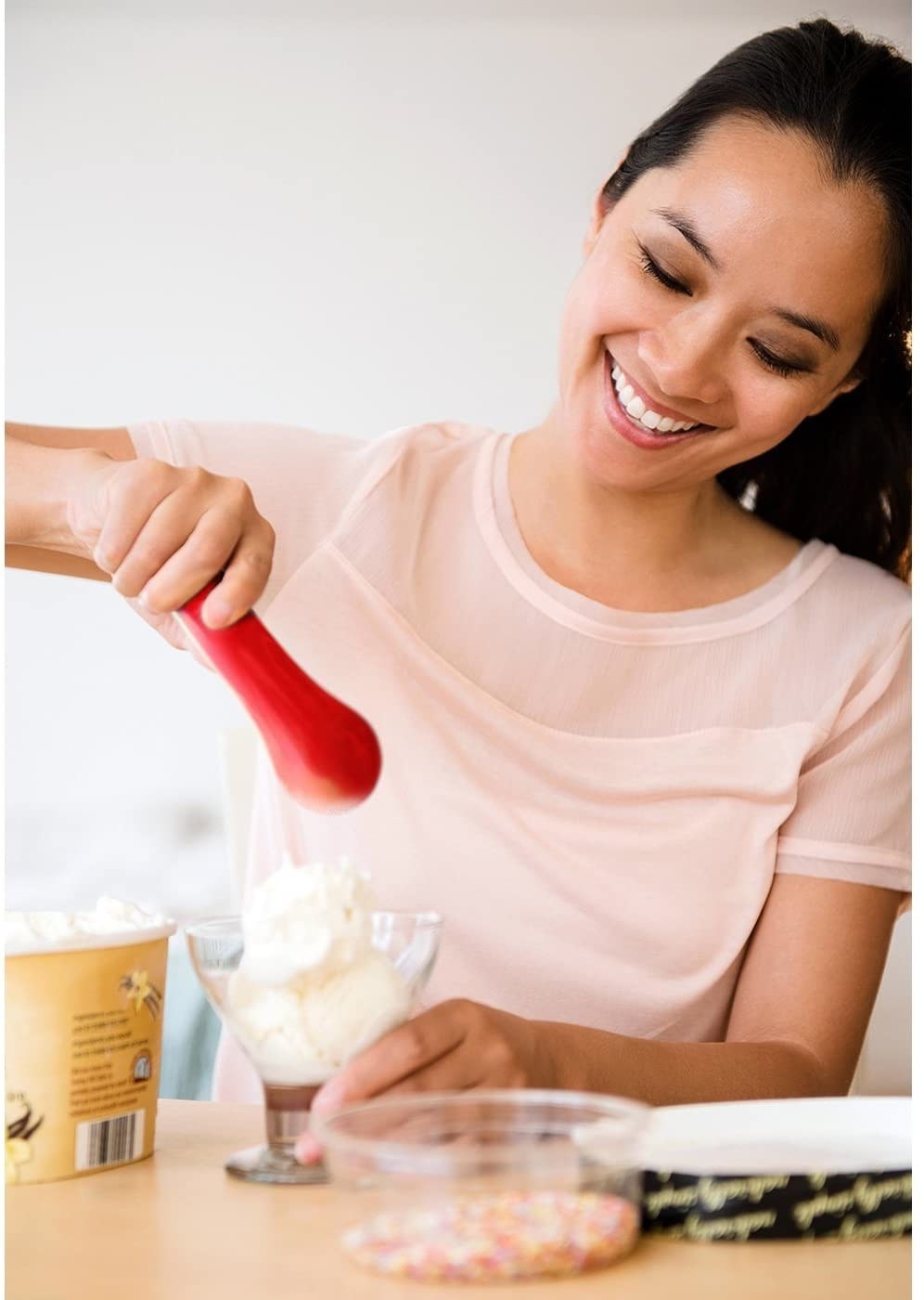 Model holding the red ice cream scoop and putting some ice cream into a cup