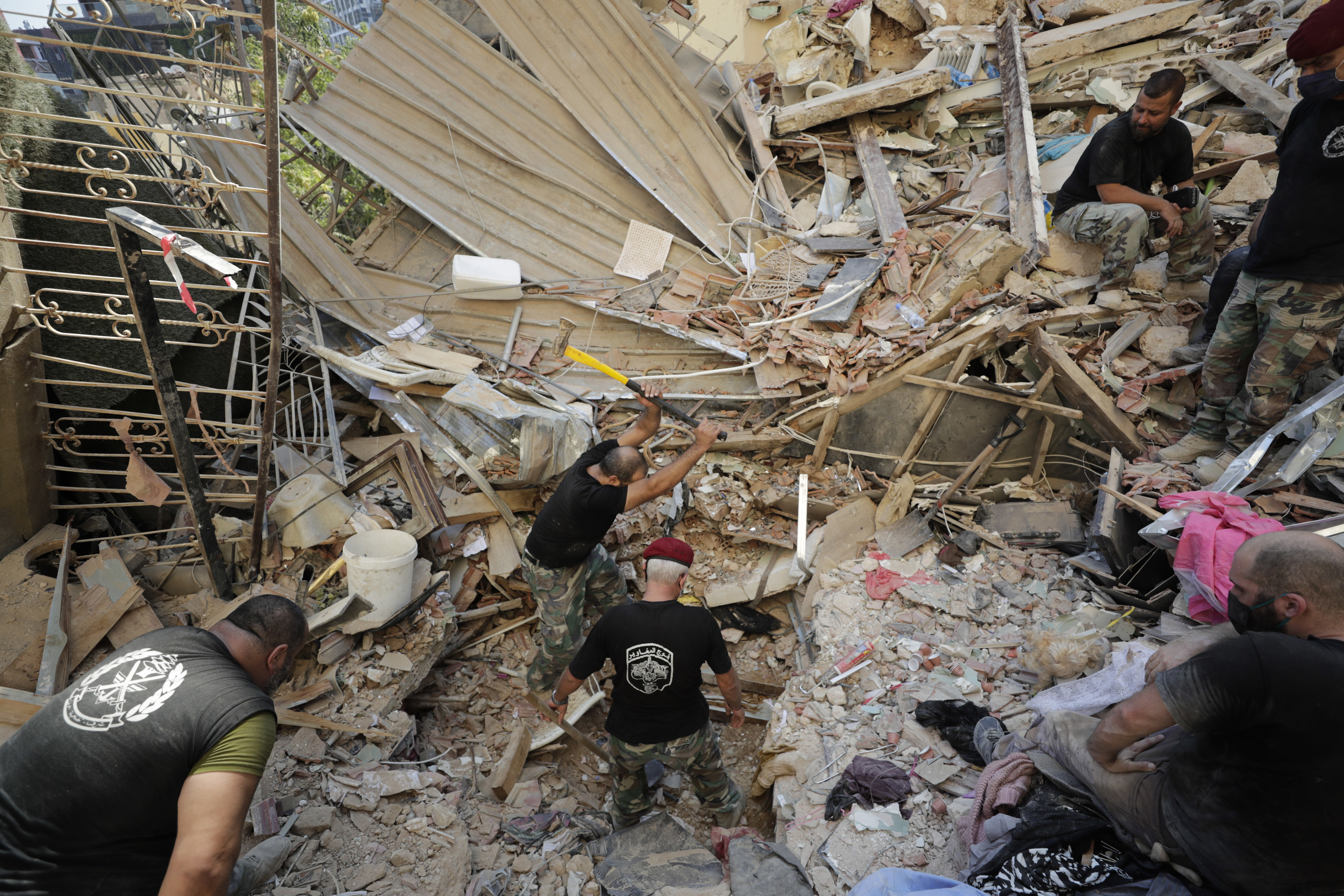 Three men in fatigues and T-shirts dig through a massive pile of rubble