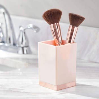 light pink container holding makeup brushes on a bathroom vanity