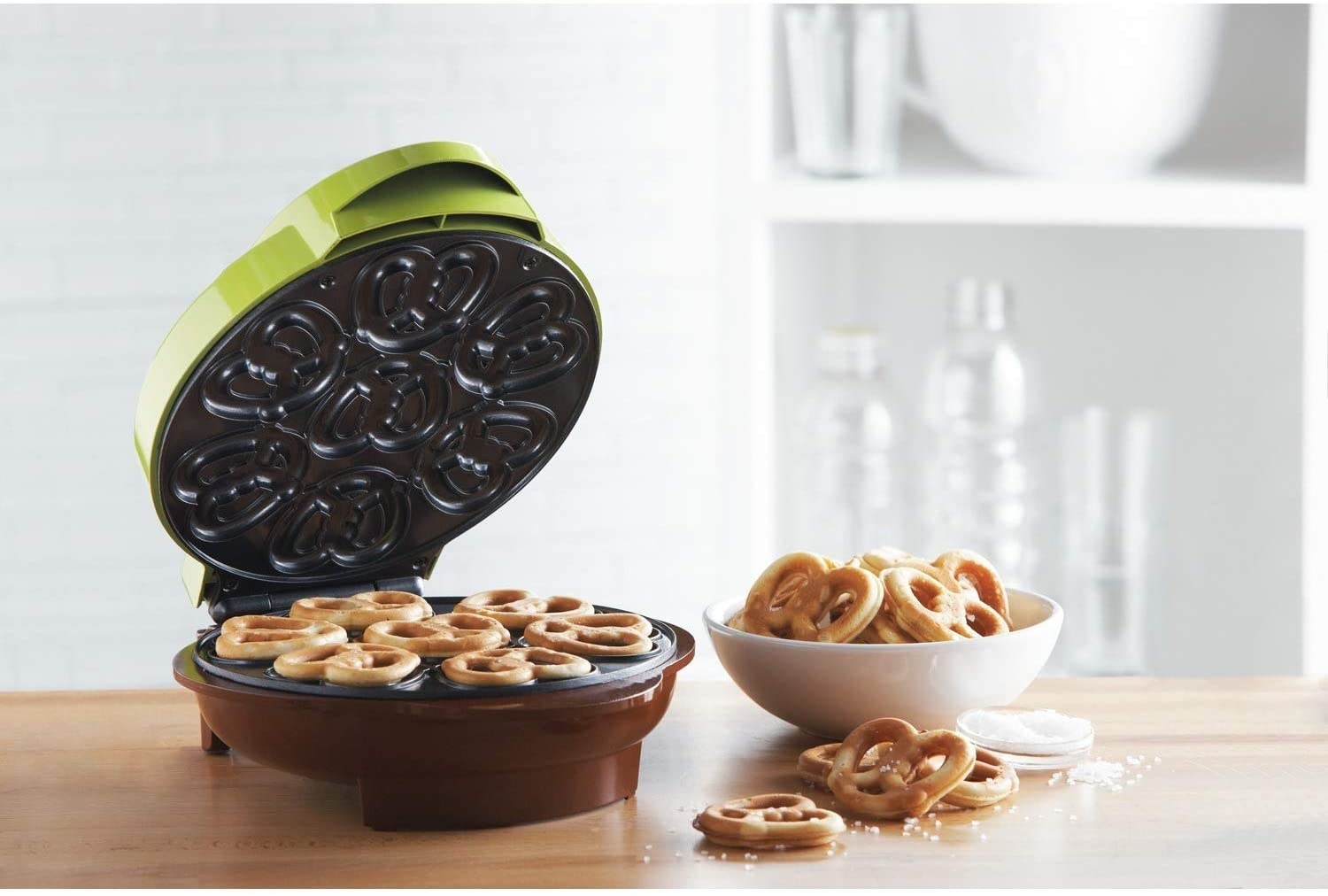 The open pretzel maker with fresh pretzels inside and a bowl of salty mini pretzels next to it