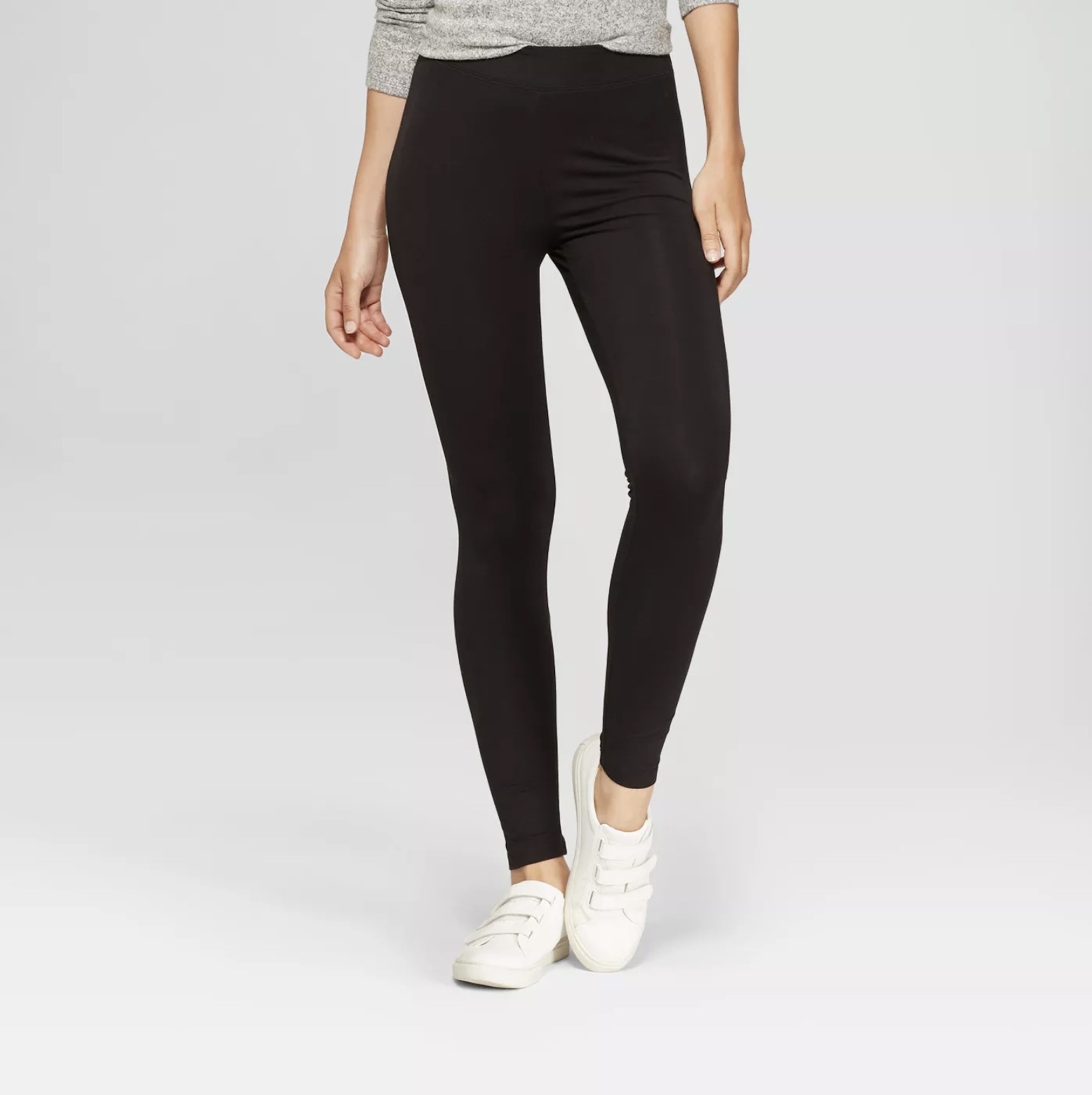 Model wears black high-rise leggings with a gray top and white sneakers