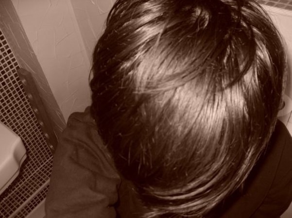 A young man holds a camera over his head and takes a close up picture from above of his hair with a big sweeping emo fringe