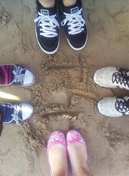 Four people stand in a circle in the sand but the photo shows only their feet