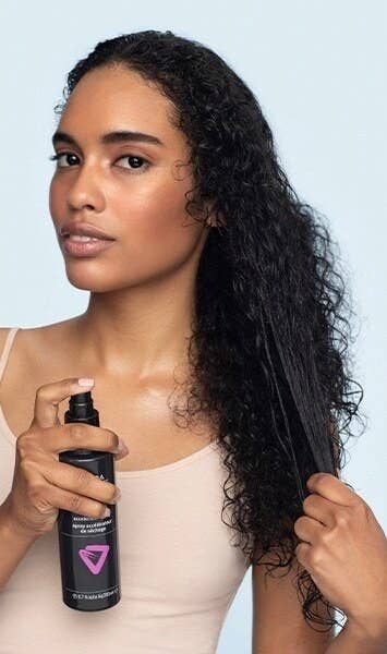 A model applying the spray to their damp, curly hair
