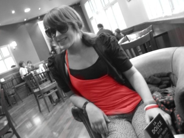 A young woman sits in a cafe that has been turned into greyscale and only her top remains brightly coloured red
