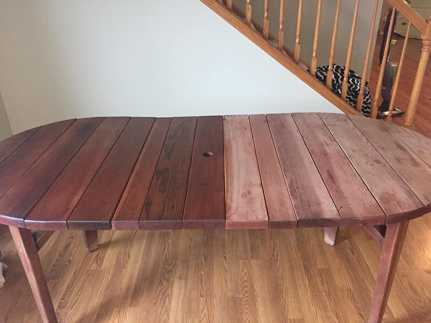 An outdoor teakwood table, half looking dried out and worn, the other half treated with the product and looking rich, hydrated, and dark