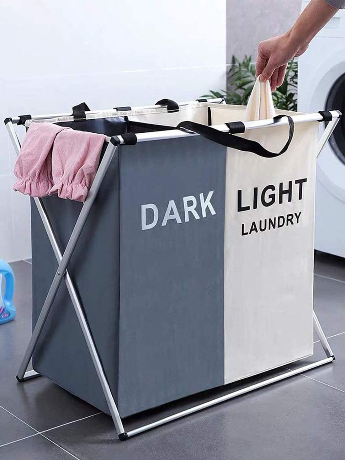 A person drops a clothing item into the light side of the divided laundry hamper