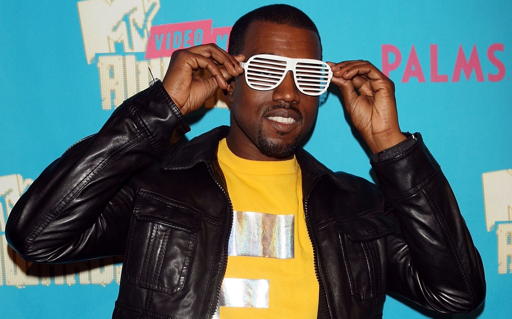 Kanye West wears a black jacket yellow t shirt and a white pair of shutter ...