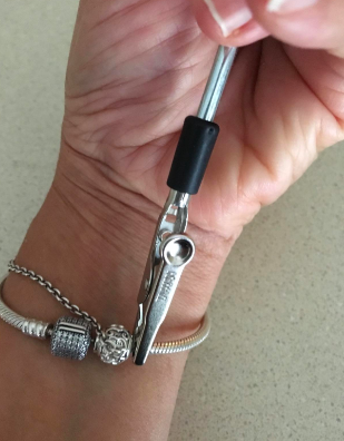 A reviewer using the tool to put a tight bracelet hook together on their own. They have the hook pinched near the clasp to easily hook it.