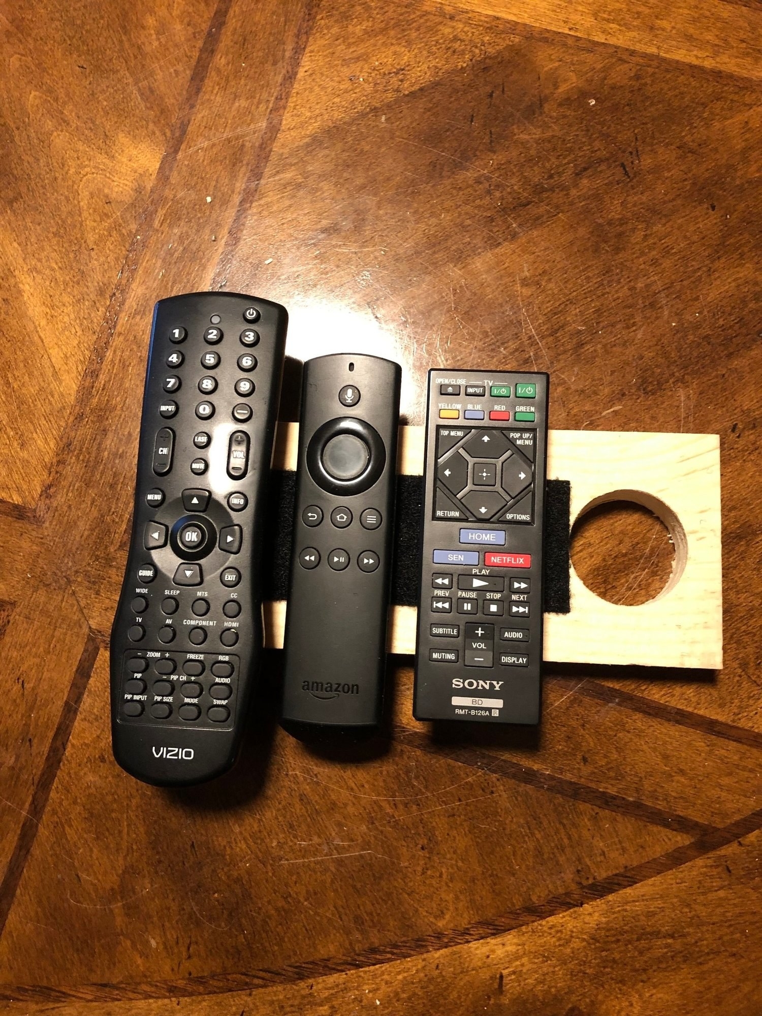 Velcro holding remote controls on a piece of wood that can hang off a doorknob