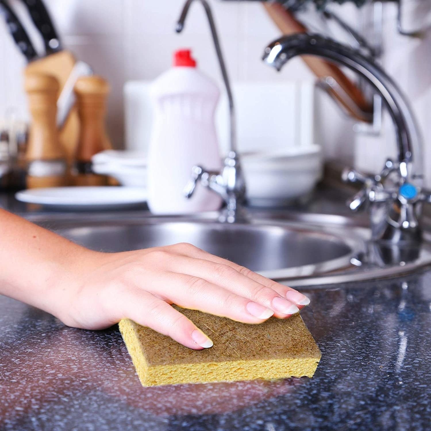 A hand holding the brown sponge while cleaning a countertop
