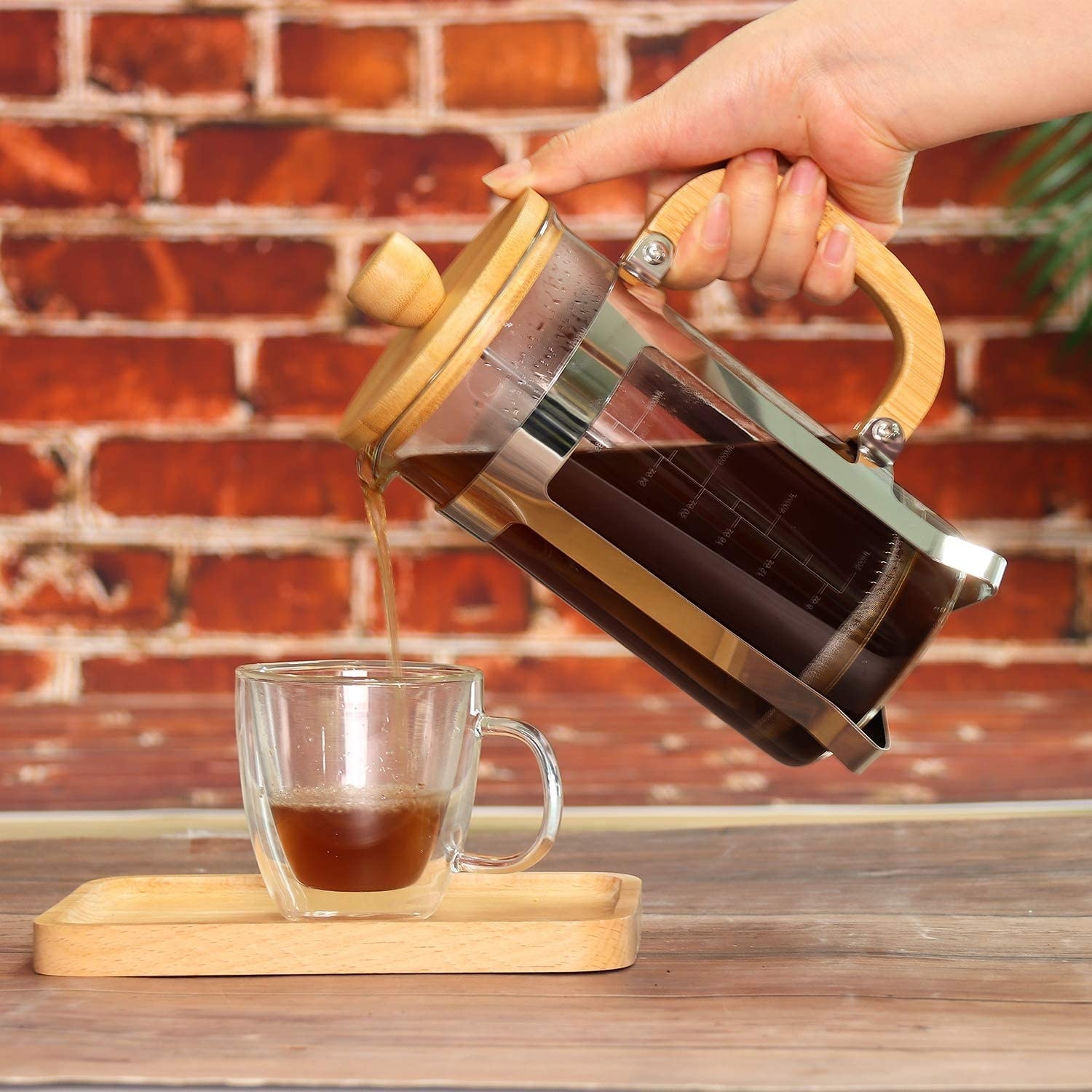 The French press with bamboo lid and handle pouring coffee into a clear coffee cup