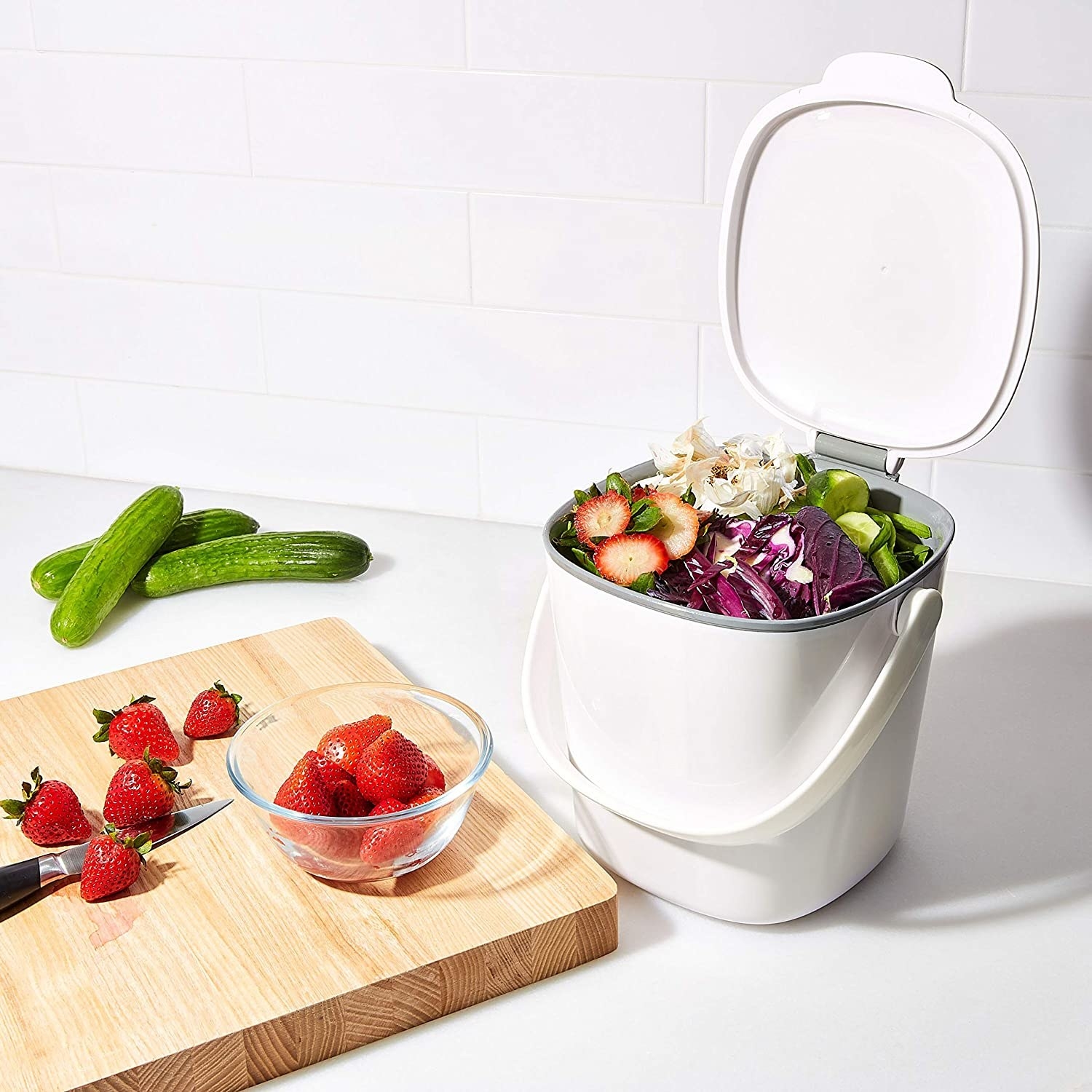 The small white compost bin with a handle and the lid open to show the food scraps inside