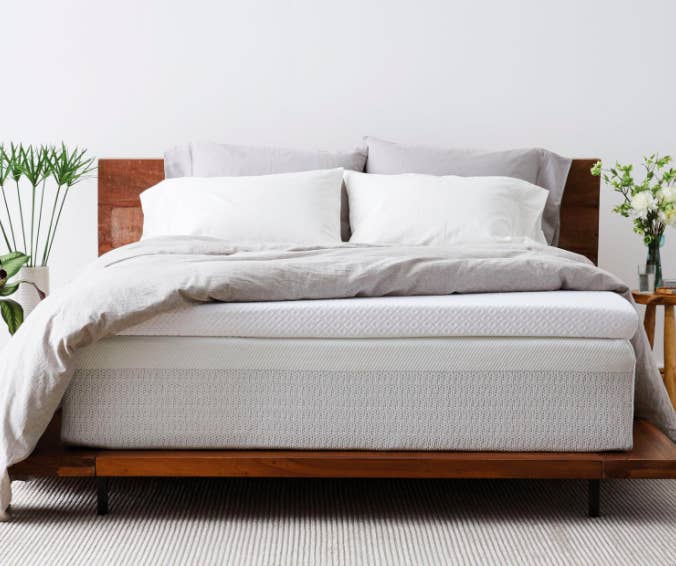 White mattress topper on top of a wooden bed with a white duvet cover 