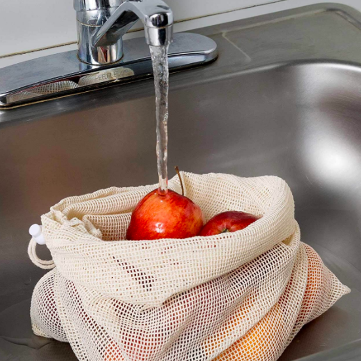 Apples being washed in the sink while staying stored inside the mesh bag