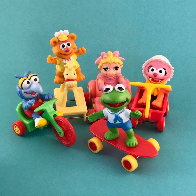 Five Muppet Babies (Gonzo, Fozzie, Piggy, Animal, and Kermit) Happy Meal toys displayed against a teal back drop. 