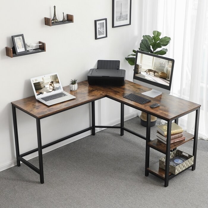 The desk, with a dark wood-like top and metal legs. On one side, the legs also have two wooden-looking shelves. It&#x27;s styled with a printer in the corner and a laptop on one side and a desktop computer on the other