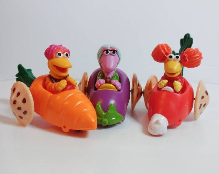 Three Fraggle Rock Happy Meal toys with the figures riding cars made of root vegetables. 
