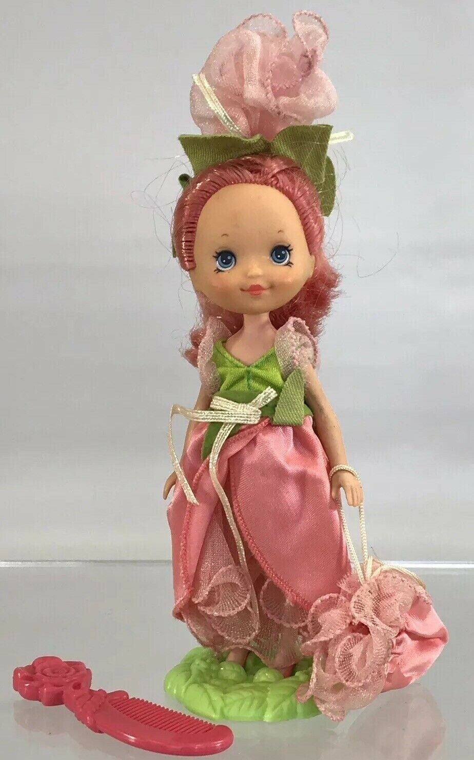 A Rose Petal doll on her stand with her pink comb to the side.
