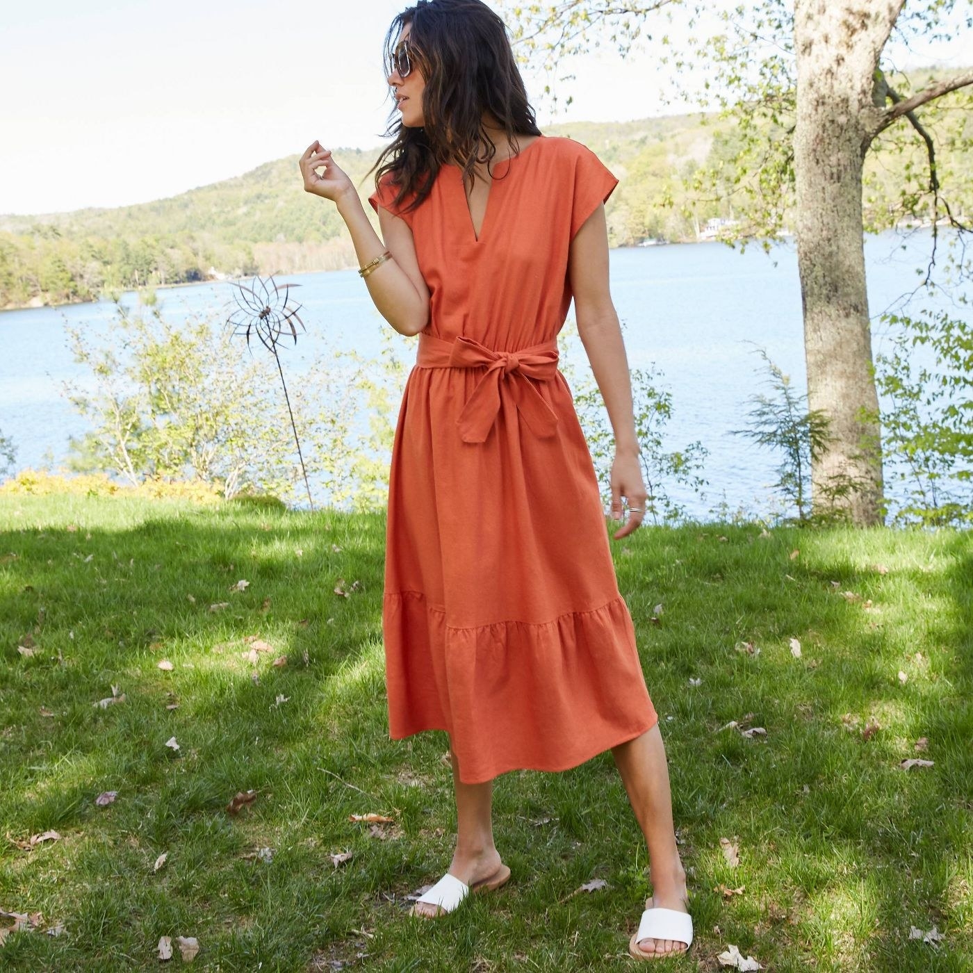 A model in an orange tie-waisted tiered dress that falls below the knee 