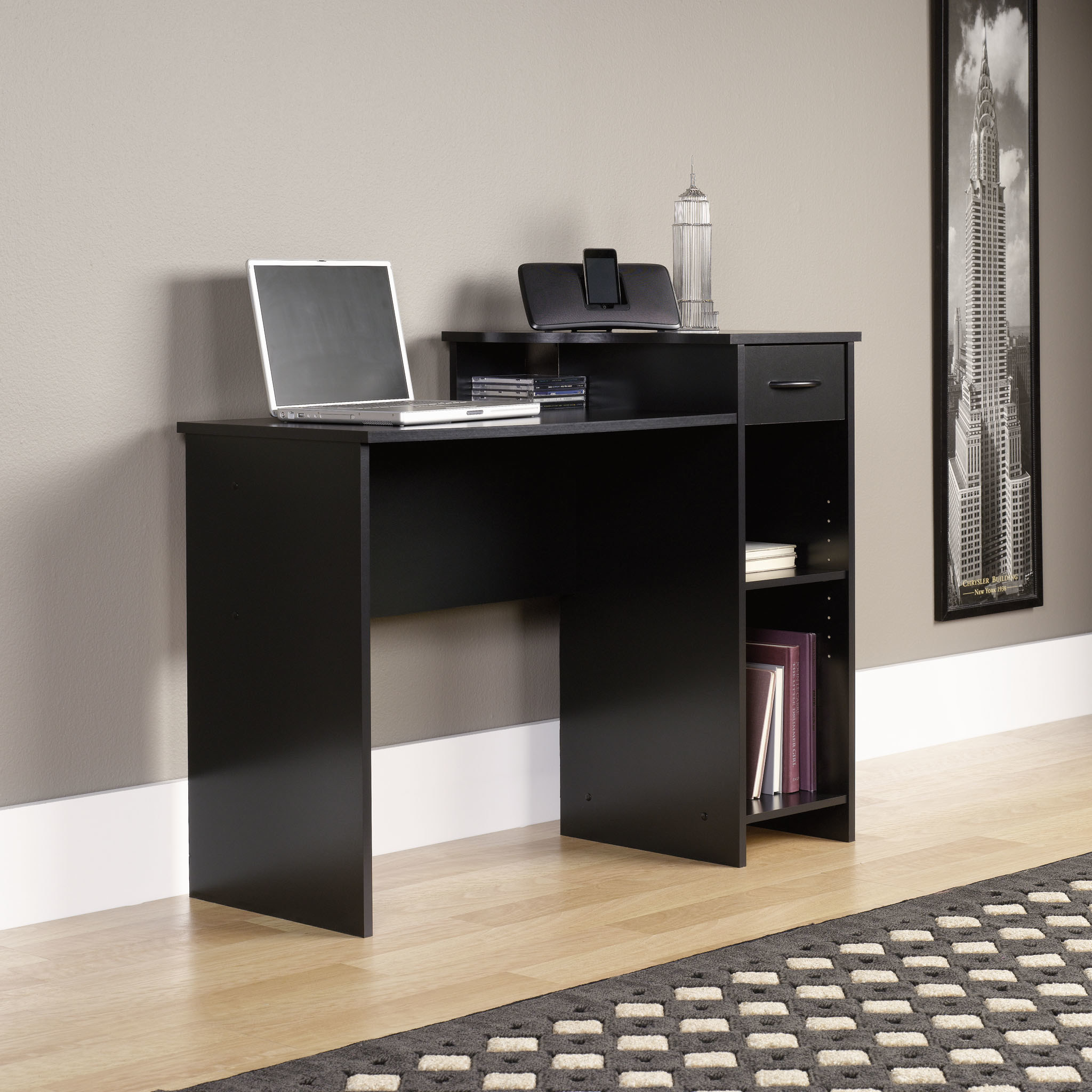 The desk is black and has a couple of storage shelves and a small drawer 