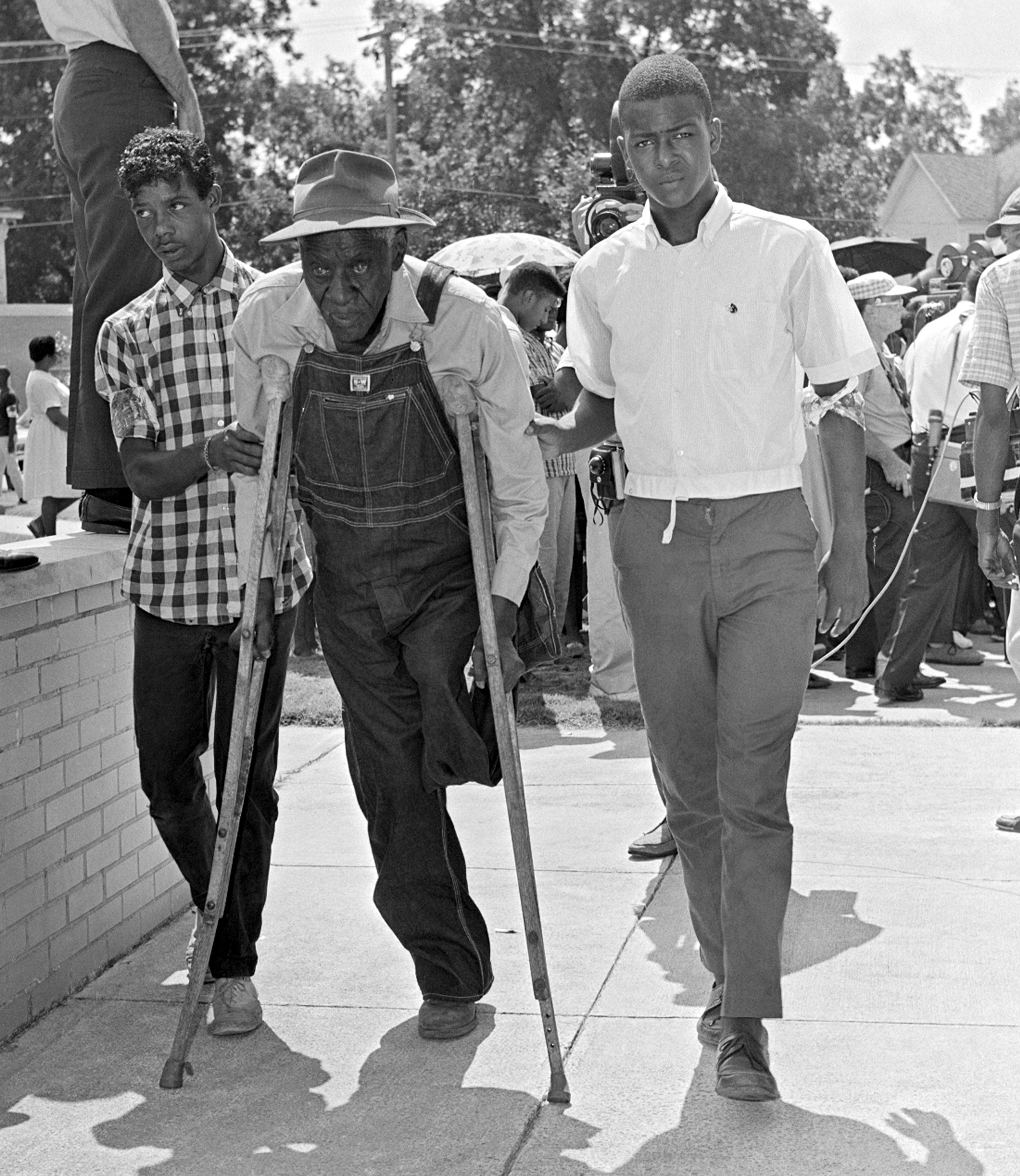 A one-legged man on crutches is helped into a courthouse by two young men 