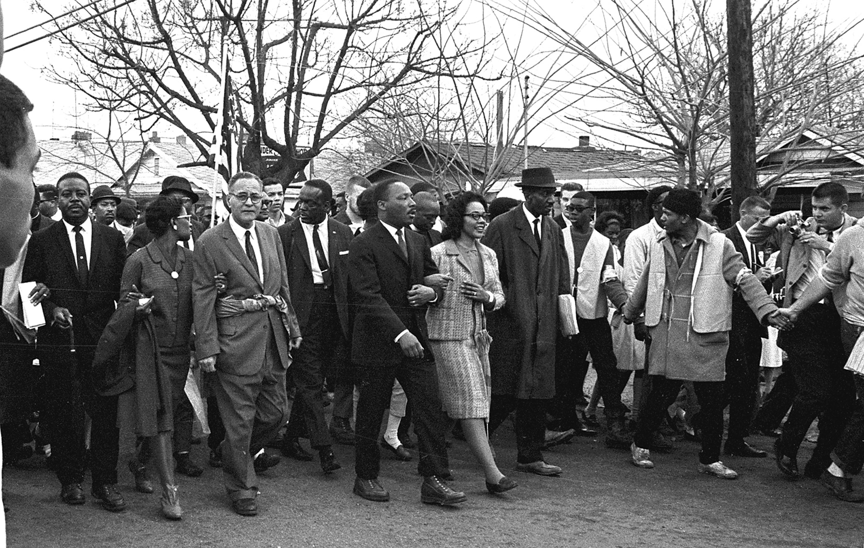 Martin Luther King Jr. and his wife lead a march of black and white people dressed nicely down the street