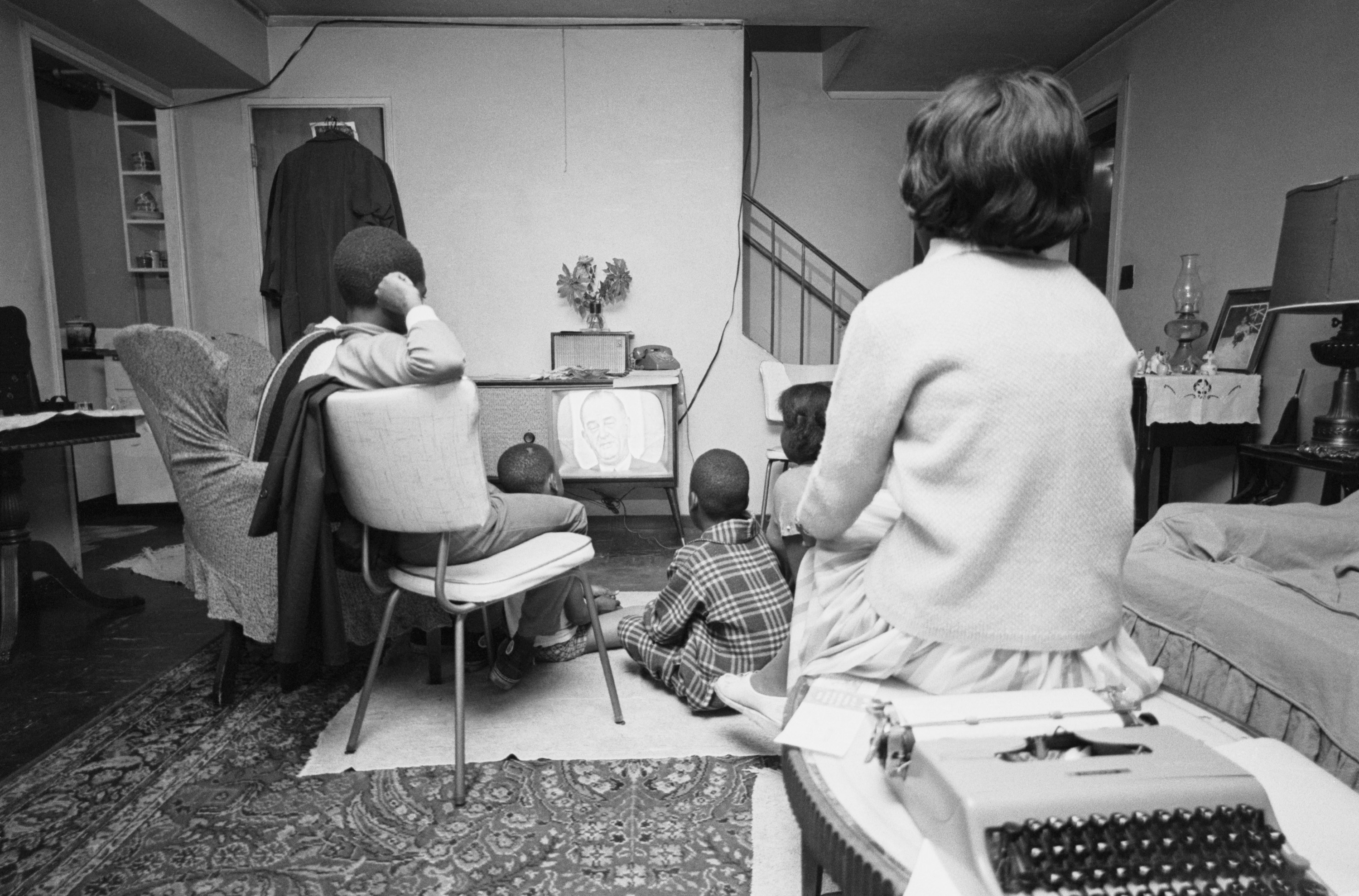 A Black family is seen in a living room watching television