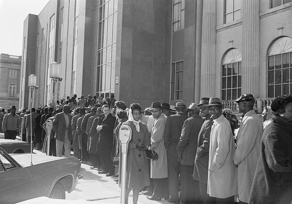 A long line of people in coats stand in front of the courthouse