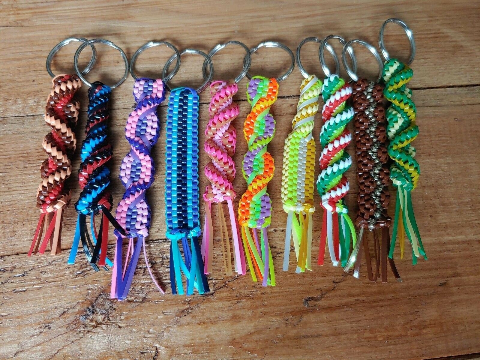 A close up image of several brightly coloured plastic keychains in which the threads have been woven into a pattern like a scoobie lying on a wooden table