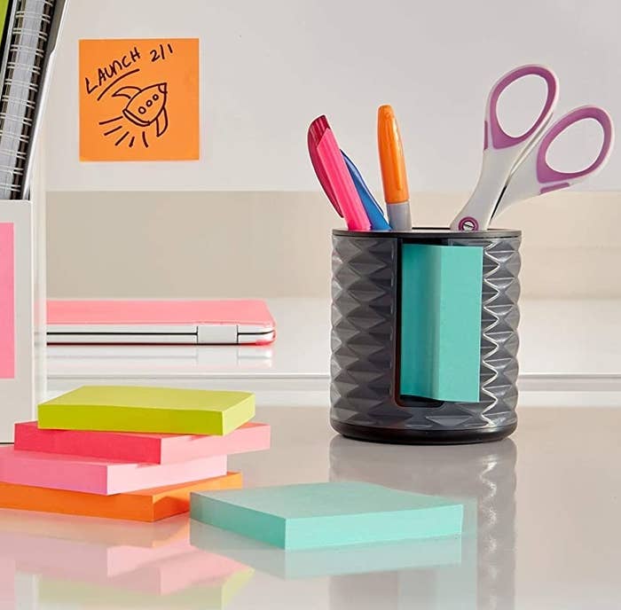 The sticky note dispenser holding markers and stickers next to a stack of sticky notes