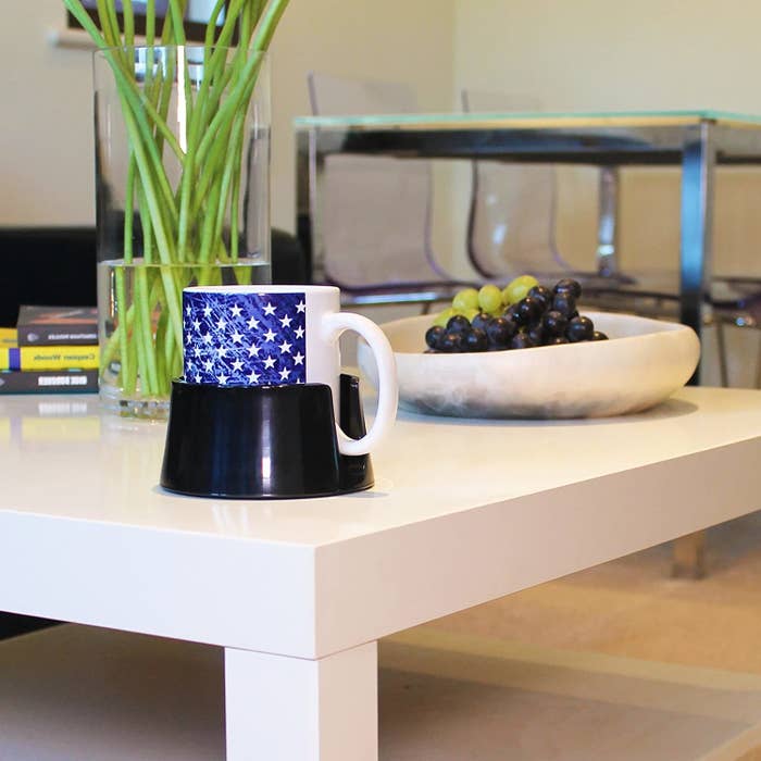 The anti-spill drink holder on a coffee table with a mug inside of it