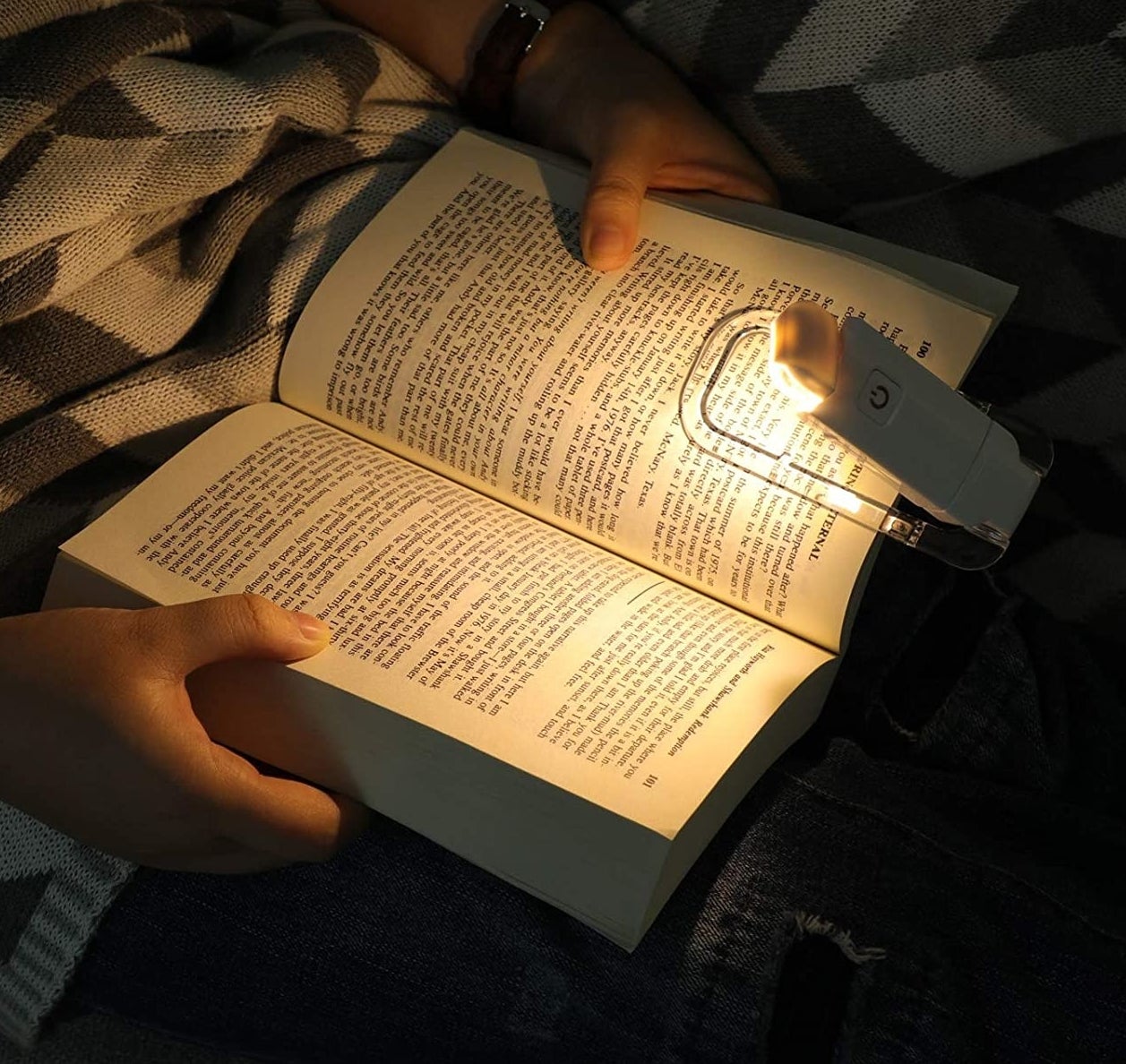 A person using the book light to illuminate the pages of their novel