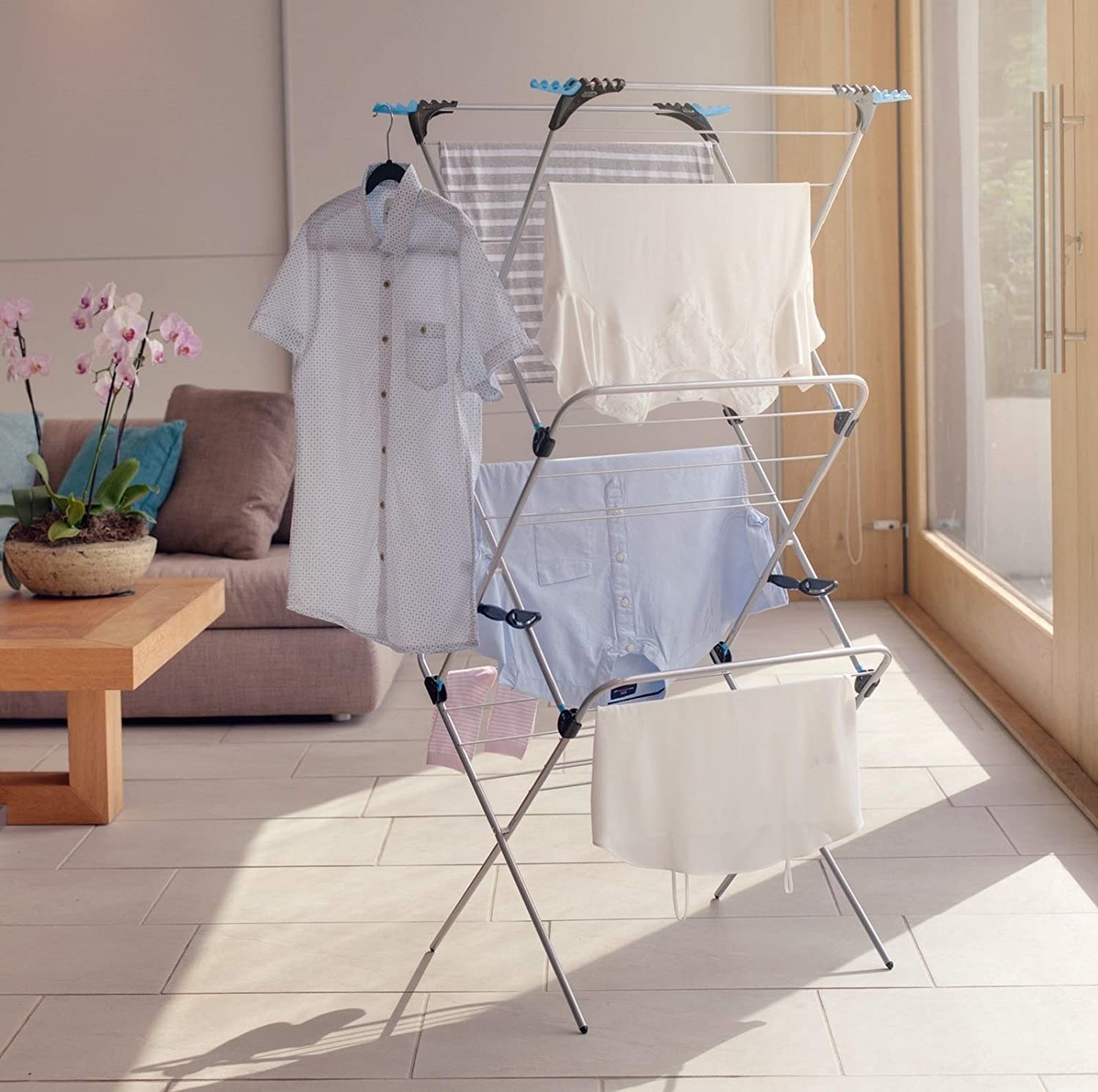 Three-tiered drying rack with clothes hanging on it in living room