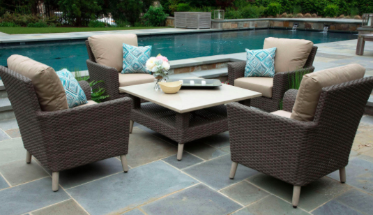 Wicker patio furniture set with four chairs and a nude-colored table near a pool