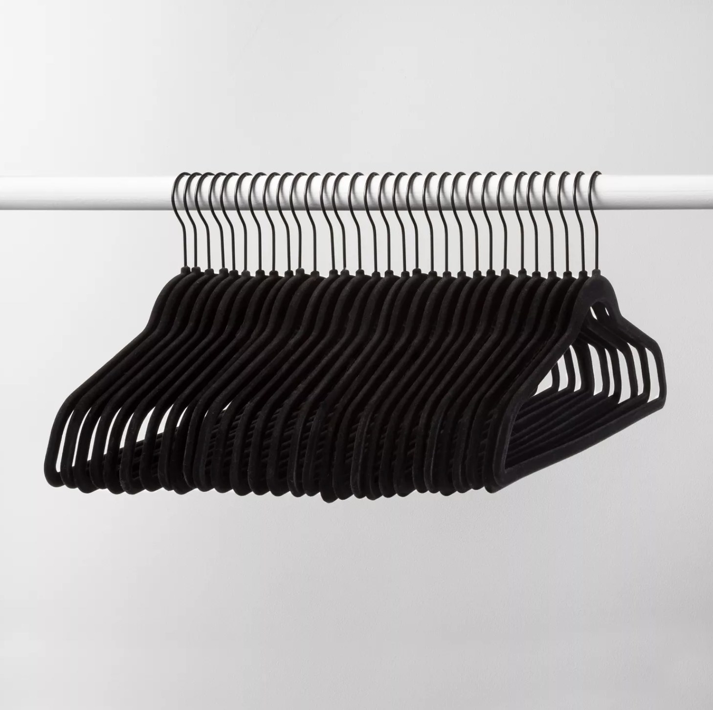 A set of 30 black velvet hangers on a white closet rod.