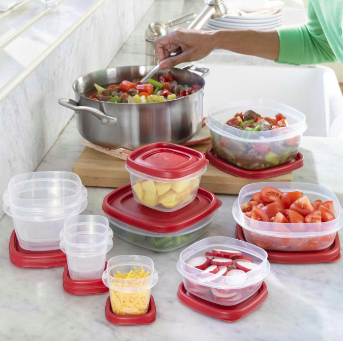 Hand holds spoon over pot next to red and clear food storage containers with fruit