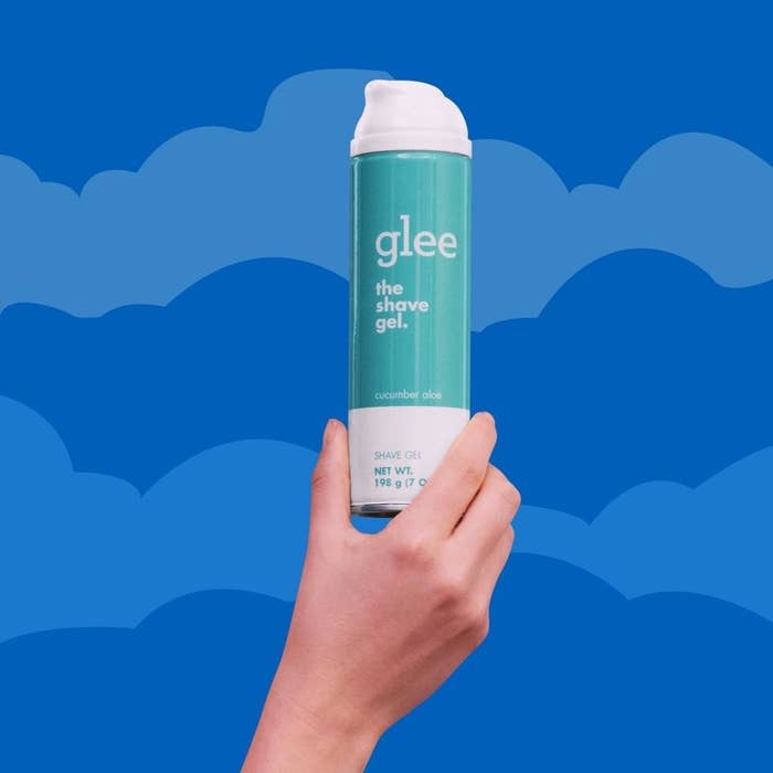 A hand holding a bottle of the shave gel against a bright background