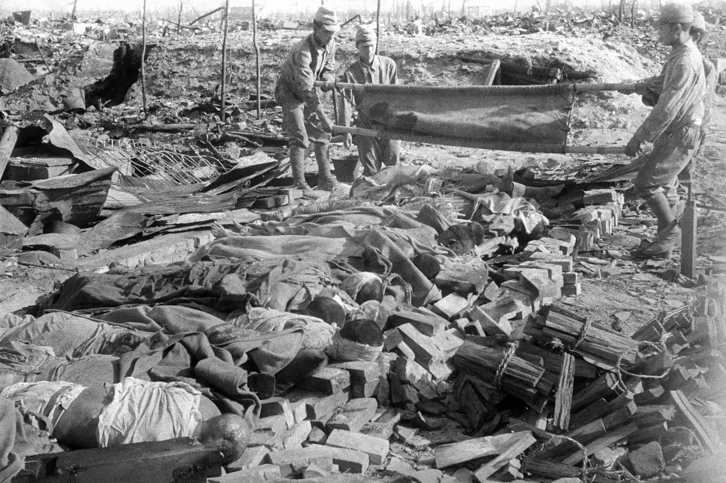 Three men tip over a stretcher, adding a corpse to a row of bodies on the ground. 