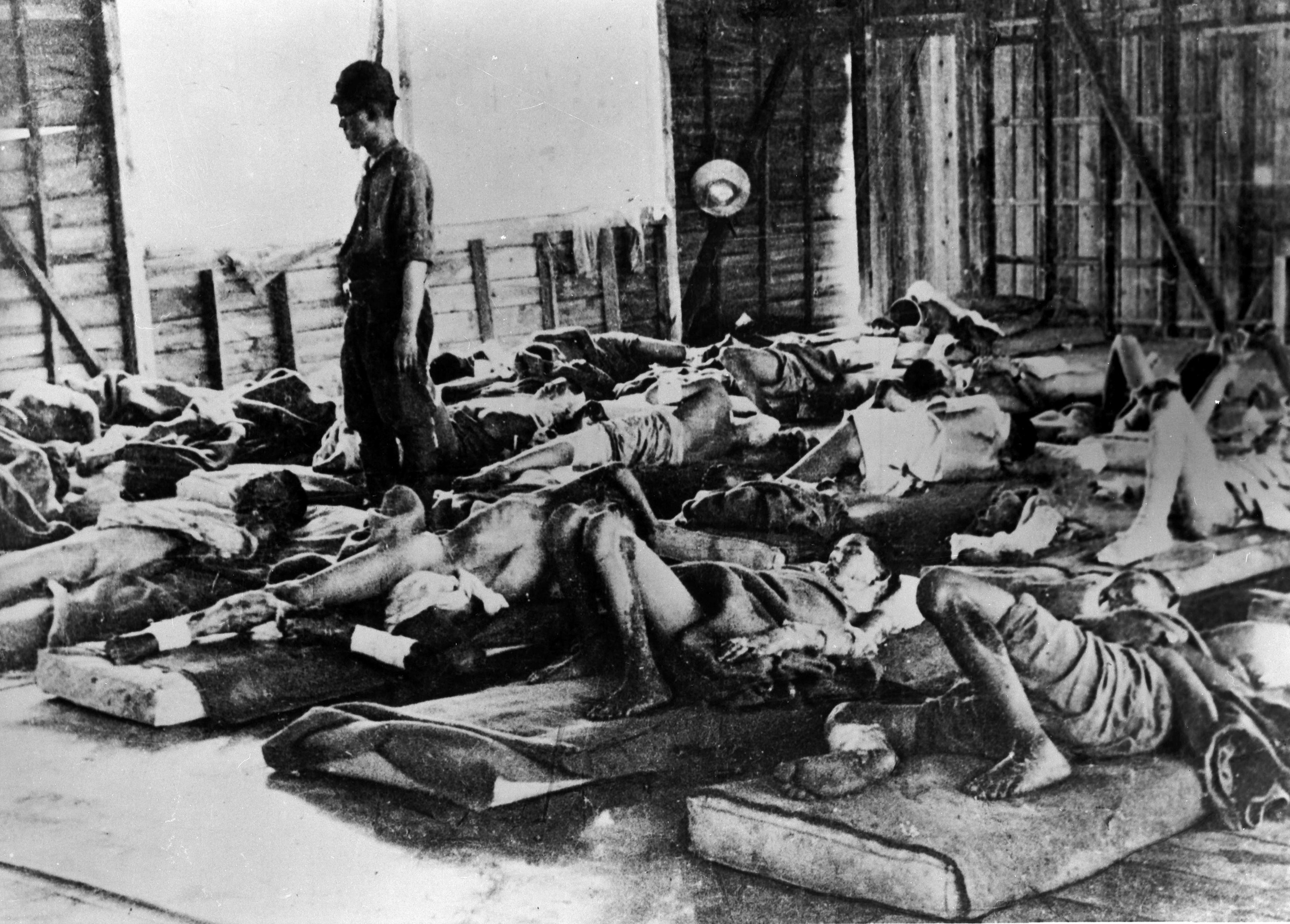 A man stands in a room packed with dozens of wounded people lying on floor mattresses