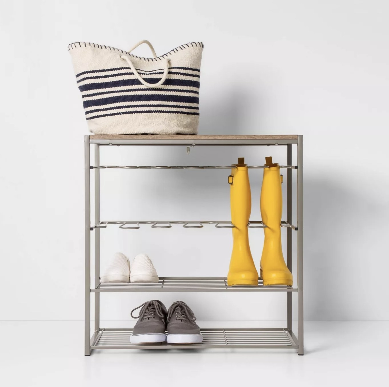 A shoe rack with two pairs of sneakers, a pair of yellow rain boots, and a large tote bag