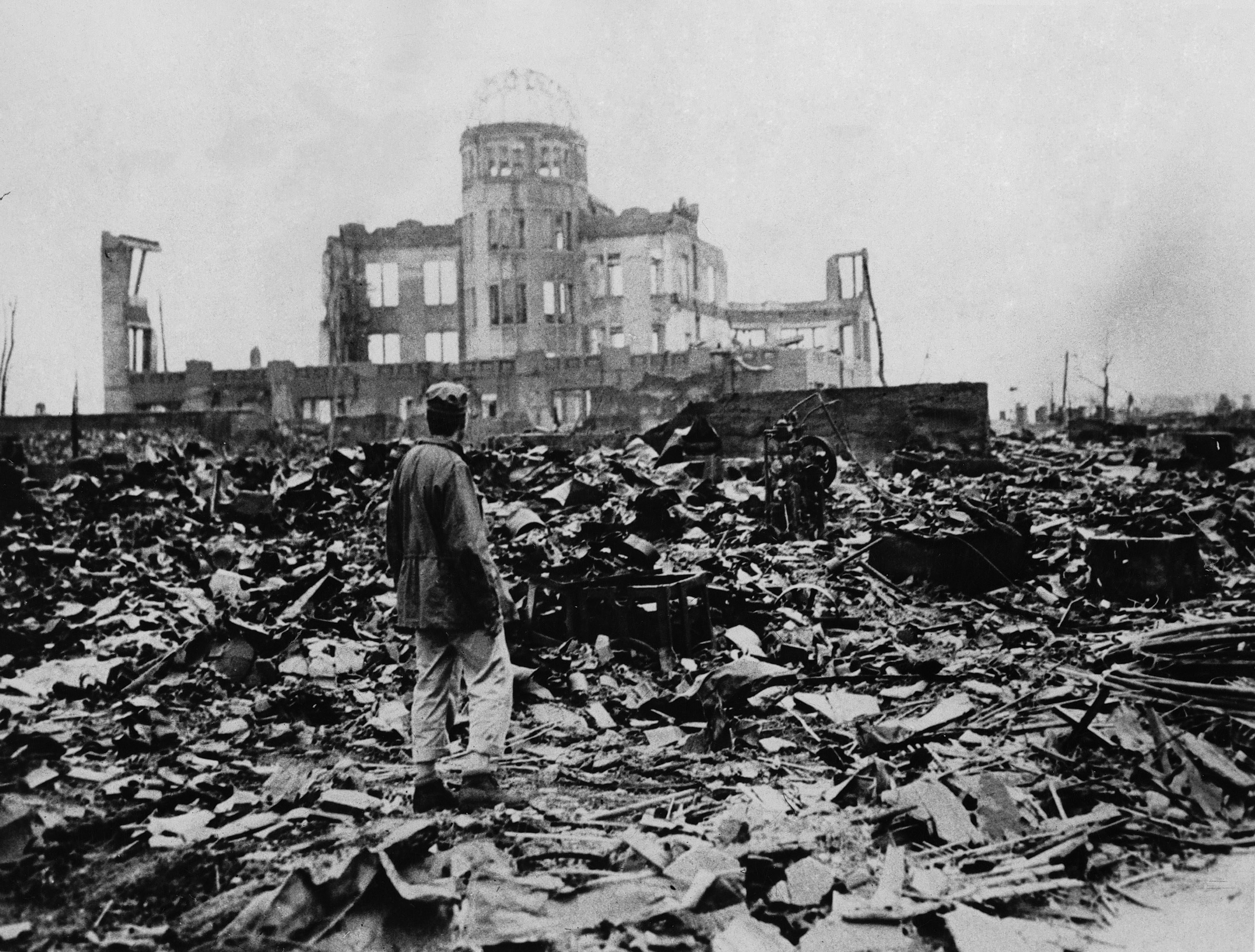 A man walks through rubble looking off to a still-standing building in the distance