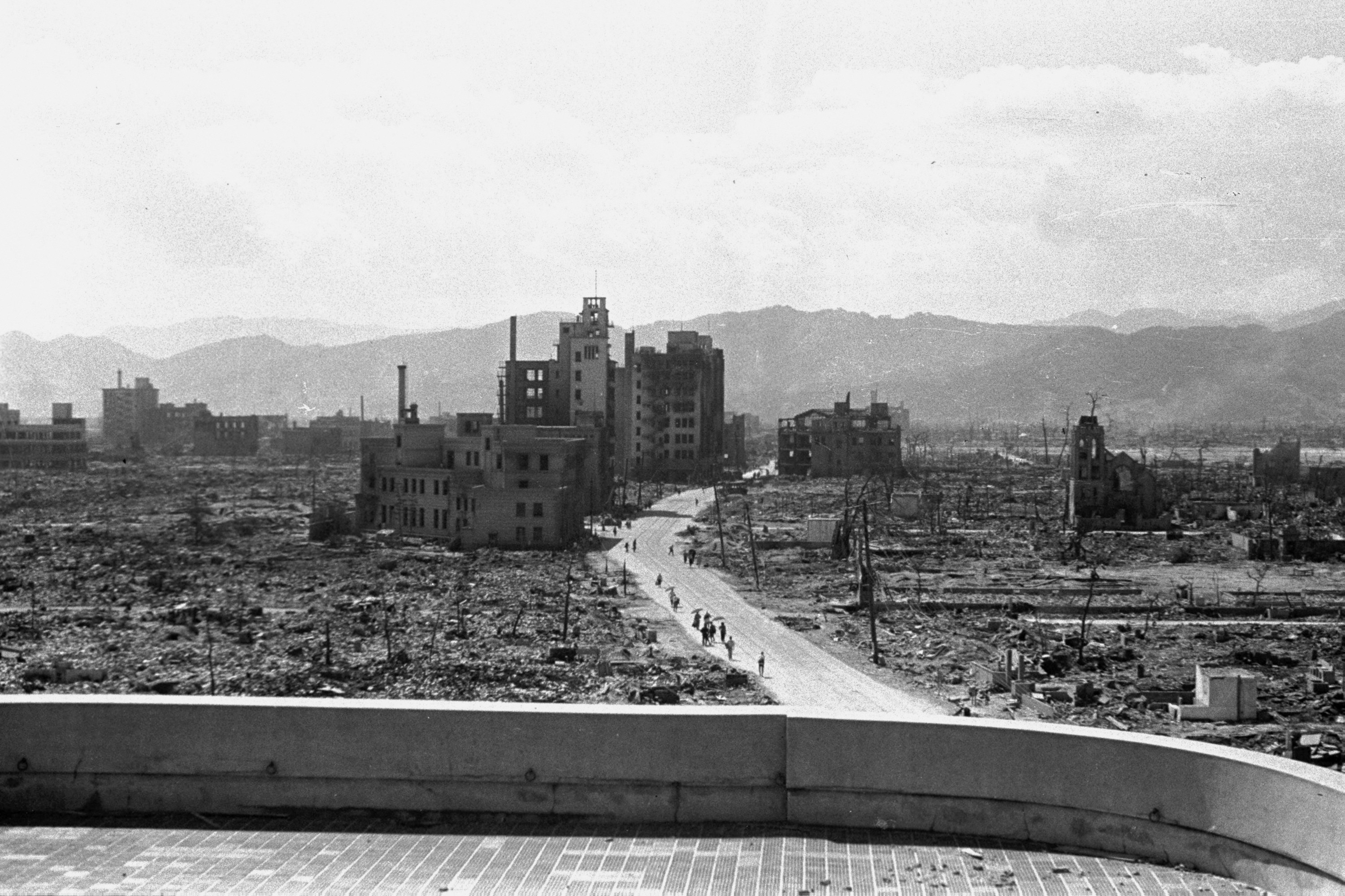 A line of people is seen walking down a desolate highway surrounded by rubble 