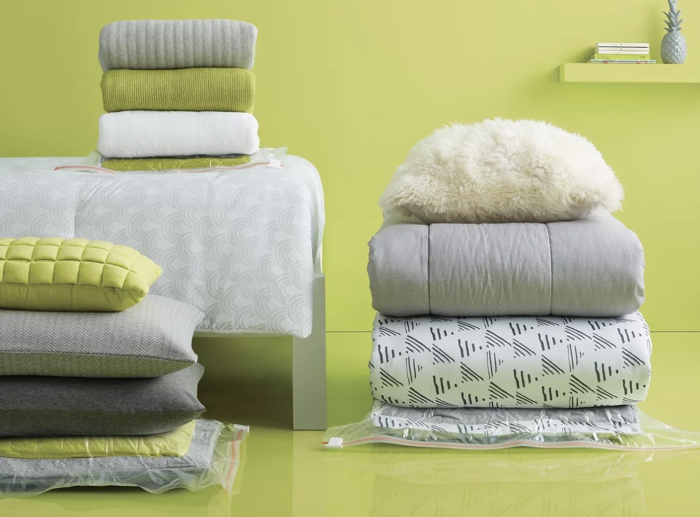 A collection of white, gray, and green bedding arranged in a green room with three items packed into compression bags